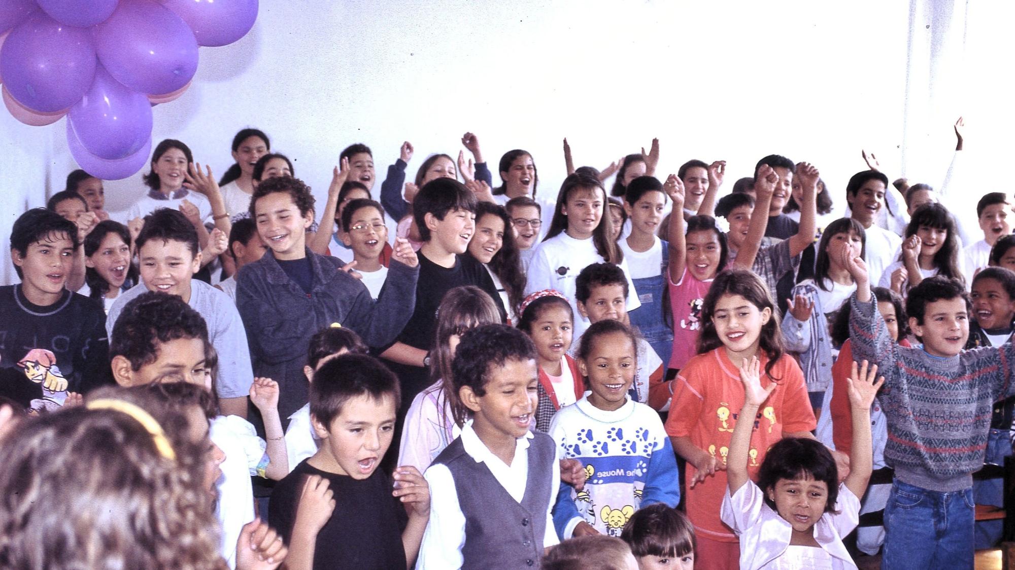 Das Foto zeigt etwa 50 Kinder, die fröhlich singen und tanzen.