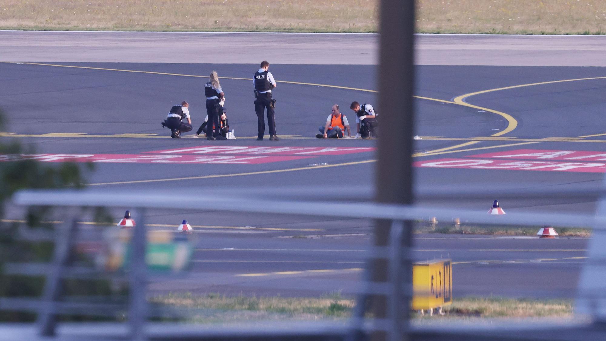 Polizistinnen und Polizisten stehen neben Mitgliedern der Klima-Gruppe Letzte Generation, die sich im Juli 2023 auf dem Rollfeld am Düsseldorfer Flughafen festgeklebt haben.