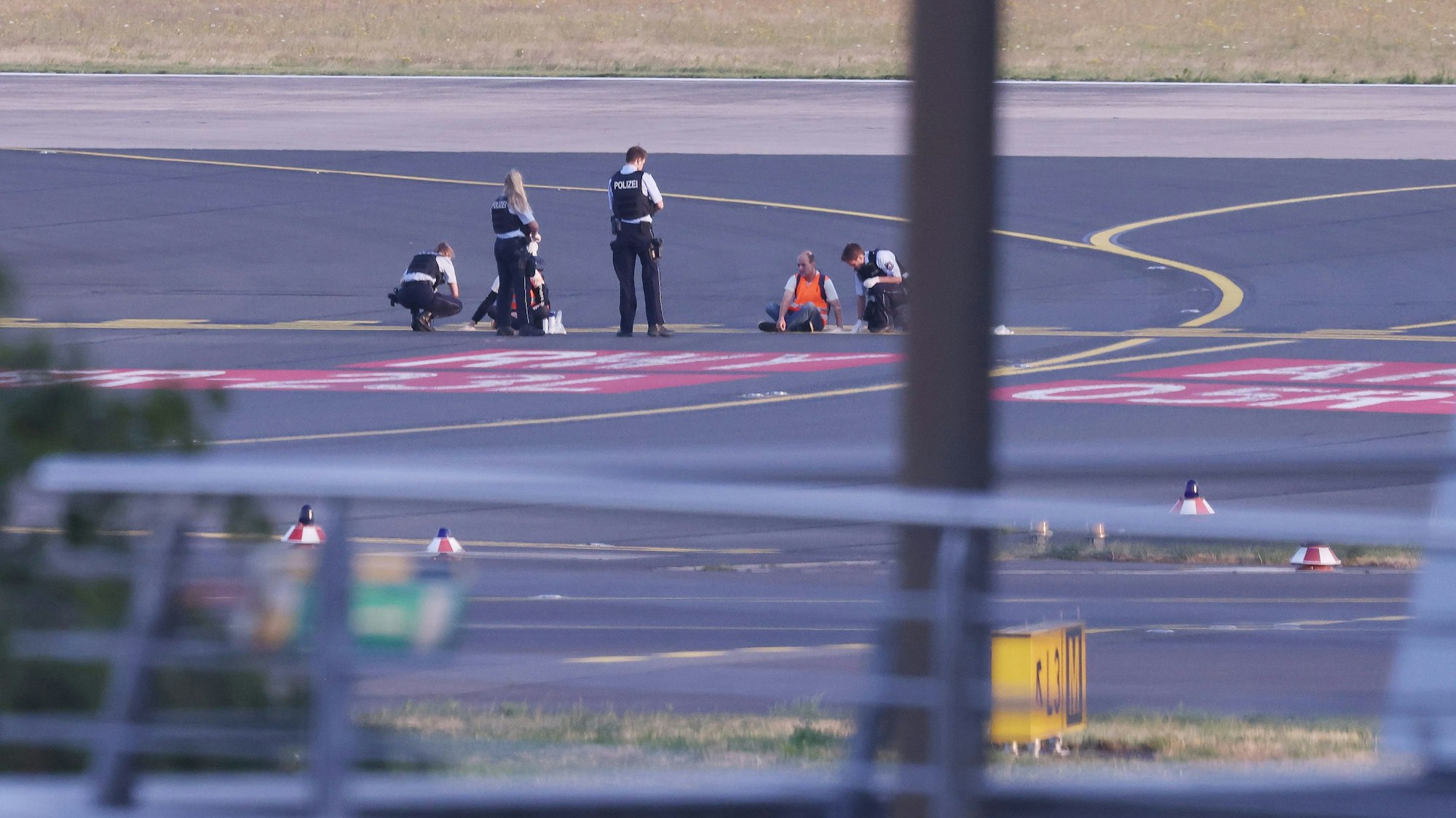 Polizistinnen und Polizisten stehen neben Mitgliedern der Klima-Gruppe Letzte Generation, die sich im Juli 2023 auf dem Rollfeld am Düsseldorfer Flughafen festgeklebt haben.