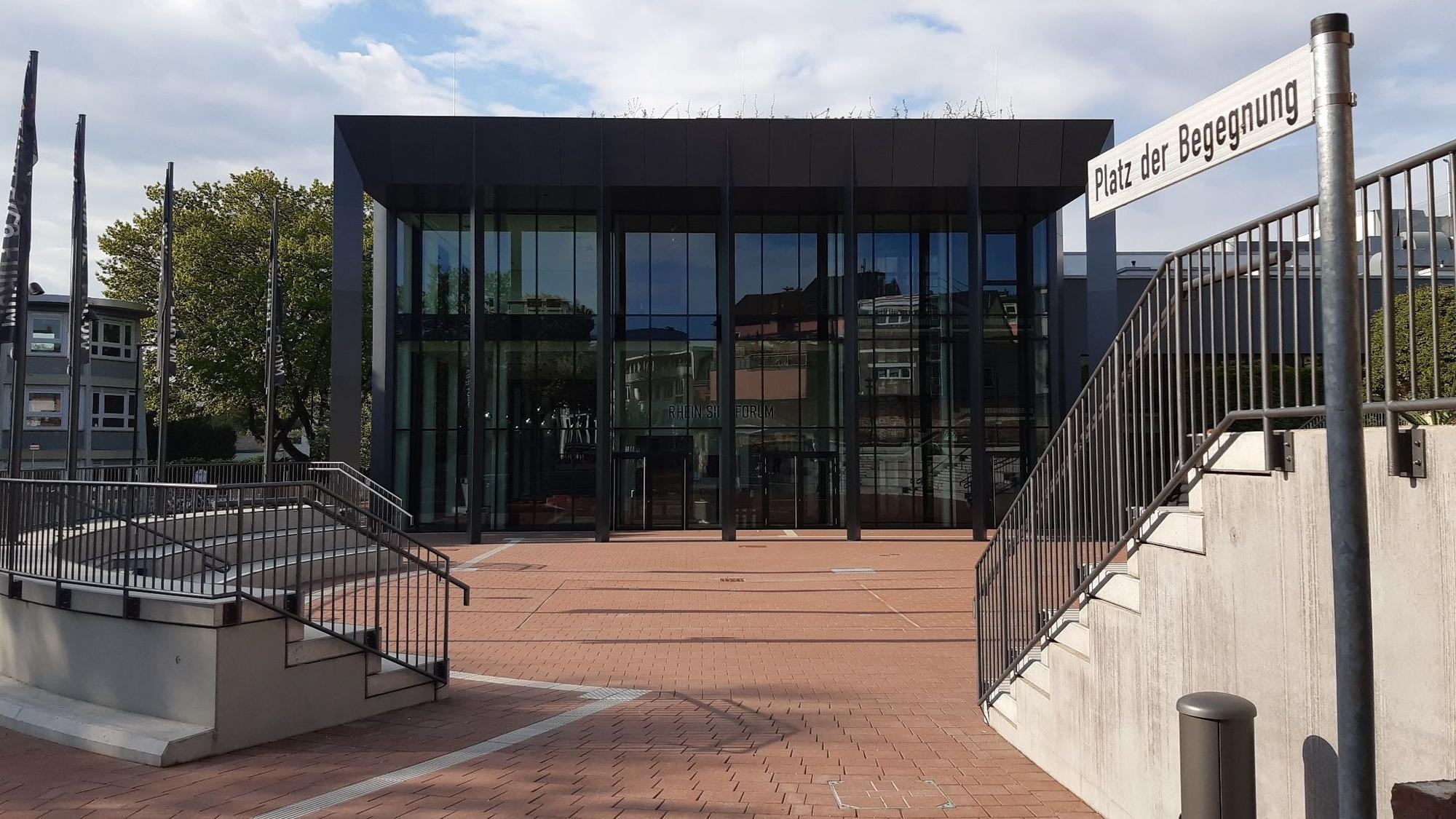 Ein Platz mit zwei kleinen Tribünen und das verglaste Foyer einer Veranstaltungshalle im Hintergrund.