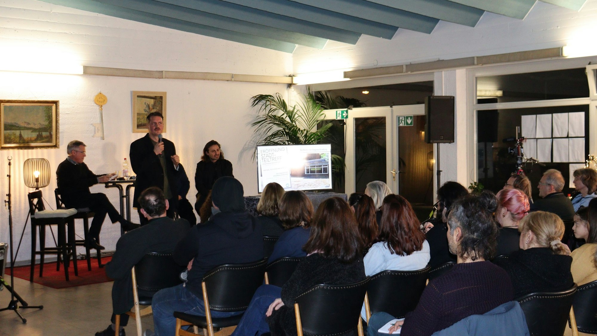 Viele Menschen sitzen in einem Saal, ein Redner spricht ins Mikrofon.