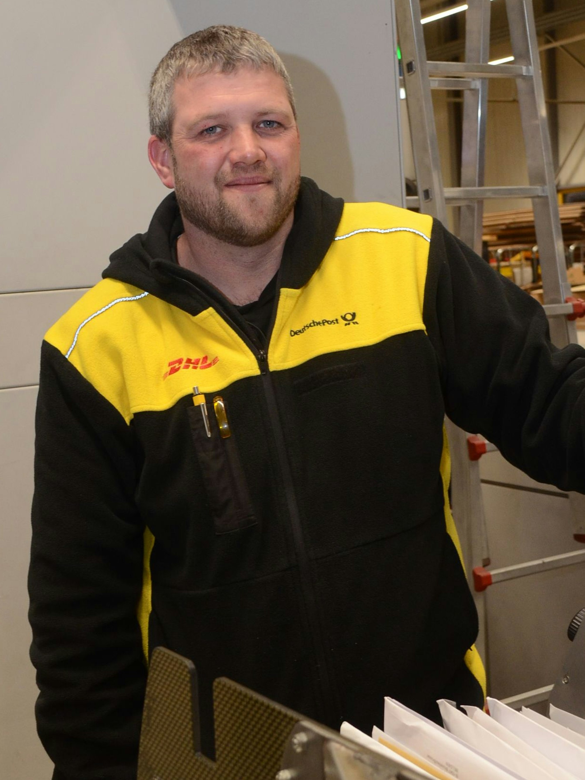 Ein Mann in einer schwarz-gelben Jacke mit Posthorn, dem Symbol der Deutschen Post, und dem roten Schriftzug DHL.