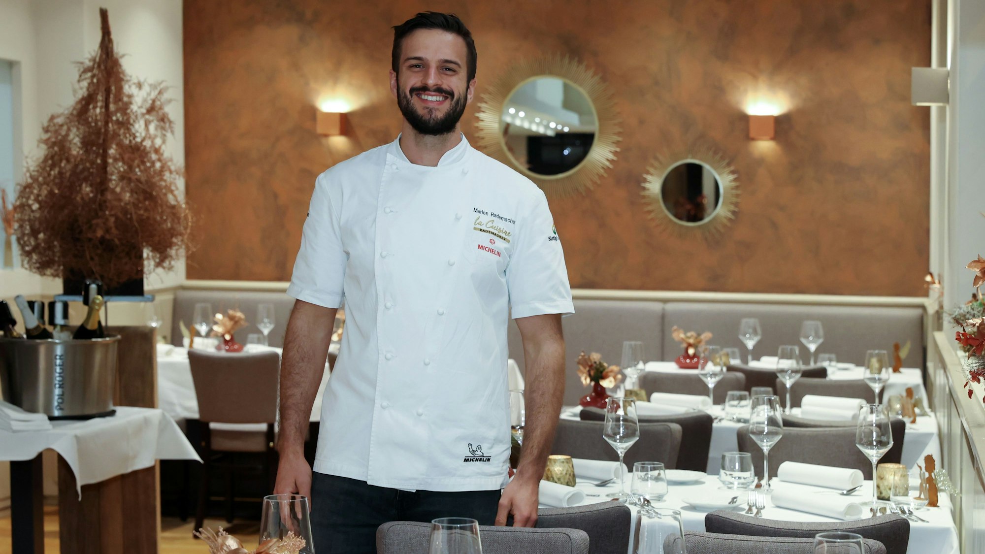 Gastronom Malon Rademacher in weißem Koch-Hemd zwischen den Tischen seines Restaurants.