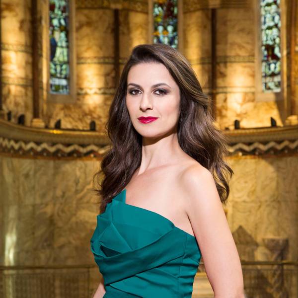 Chen Reiss trägt ein grünes Kleid und hat lange, gewellte braune Haare. Hinter ihr eine marmorne Wand eines alten Gebäudes.