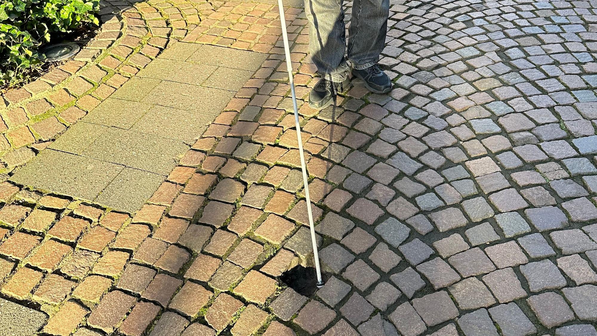 Günther Heger findet mit seinem Blindenstock ein Loch im Pflaster des Weges. Eine mögliche Stolperfalle.