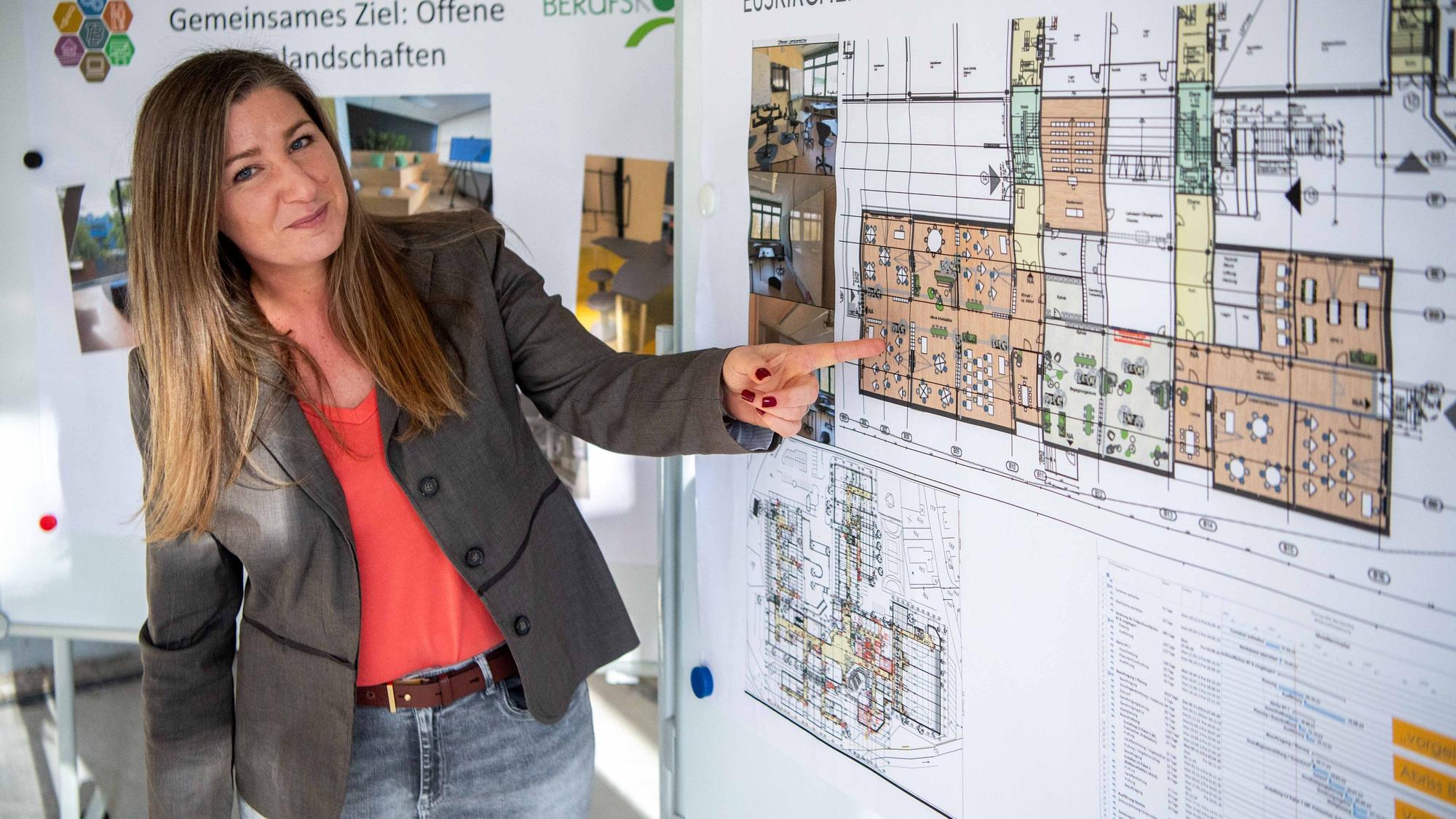 Nadine Schmitz steht vor einer Stellwand und zeigt mit ihrer linken Hand auf einen Plan.