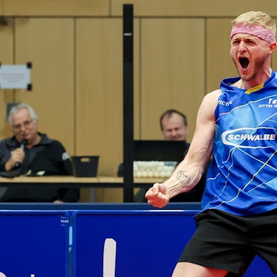 Tischtennis-Profi Romain Ruiz steht an einer Tischtennisplatte und jubelt lautstark.