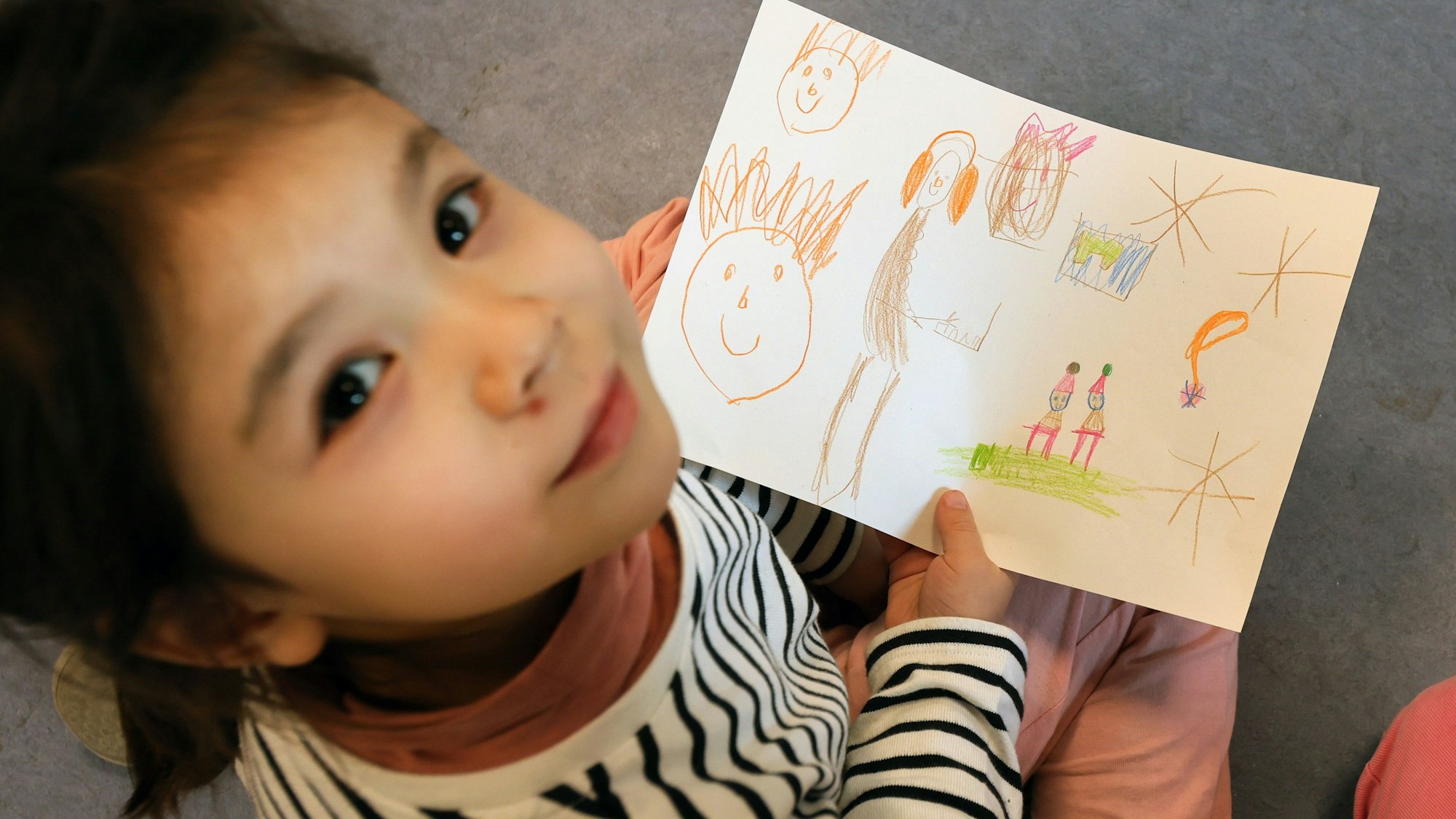 Ein Mädchen hält einen gemalten Wunschzettel in der Hand und blickt in die Kamera.