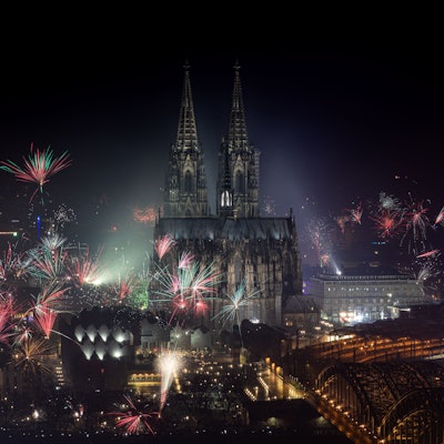 Feuerwerk explodiert zum Jahreswechsel rund um den Kölner Dom, dieser und die Hohenzollernbrücke ist angeleuchtet.