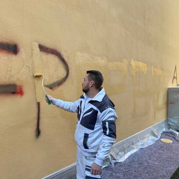 Zu sehen ist ein Maler, der Gaffiti an der Rathausfassade überstreicht.