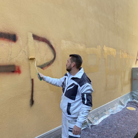 Zu sehen ist ein Maler, der Gaffiti an der Rathausfassade überstreicht.