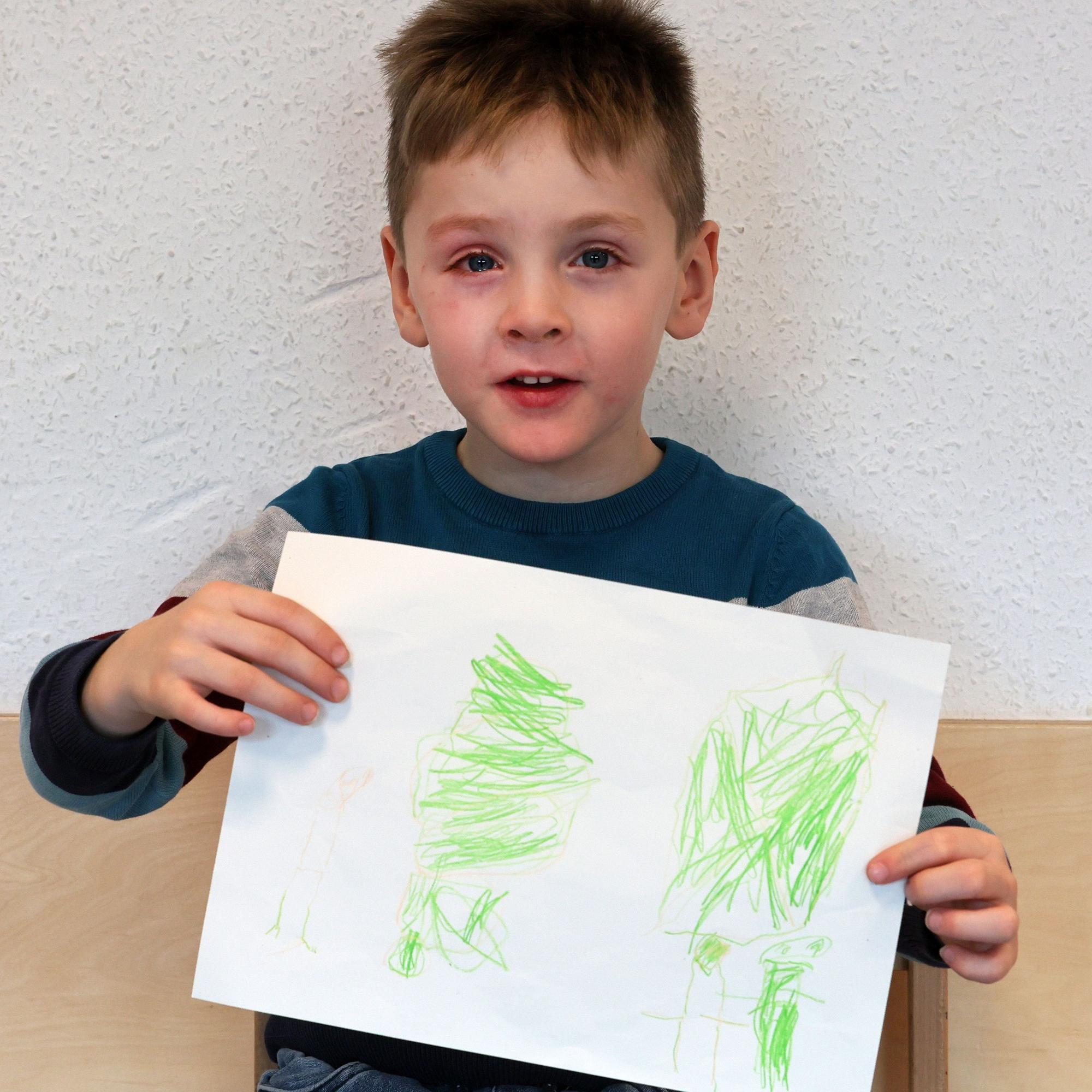 Ein Junge hält einen gemalten Wunschzettel in der Hand und blickt in die Kamera.