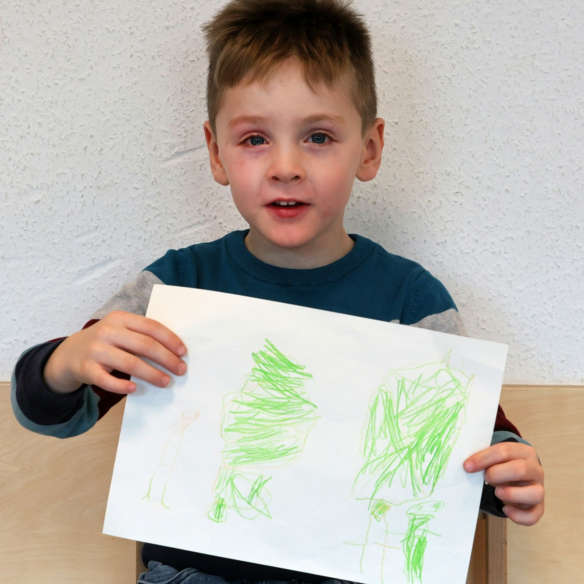 Ein Junge hält einen gemalten Wunschzettel in der Hand und blickt in die Kamera.