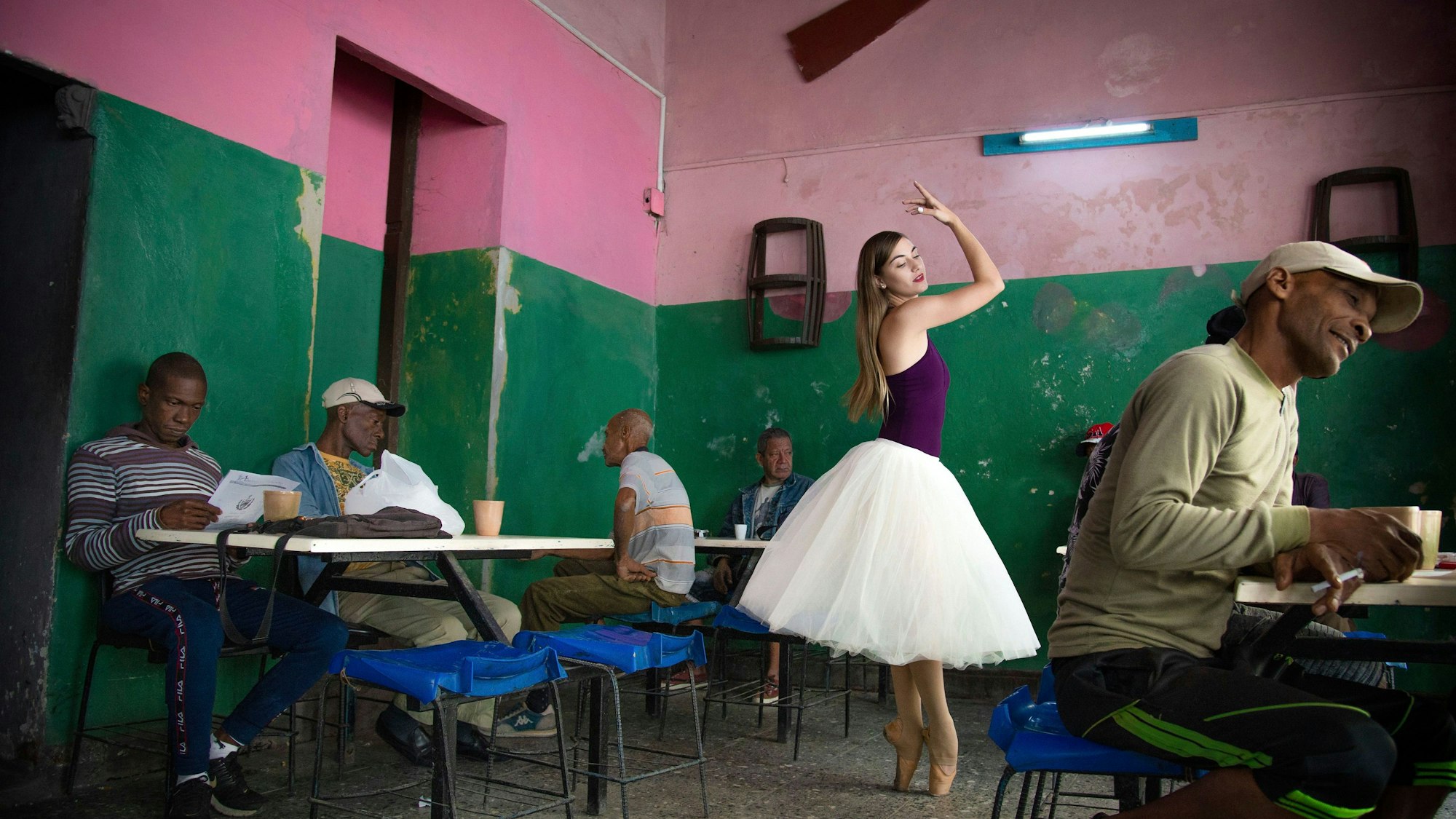 In einem kubanischen Café sitzen einige Männer und trinken Kaffee. In ihrer Mitte tanzt eine junge Frau mit weißen Tüllrock.