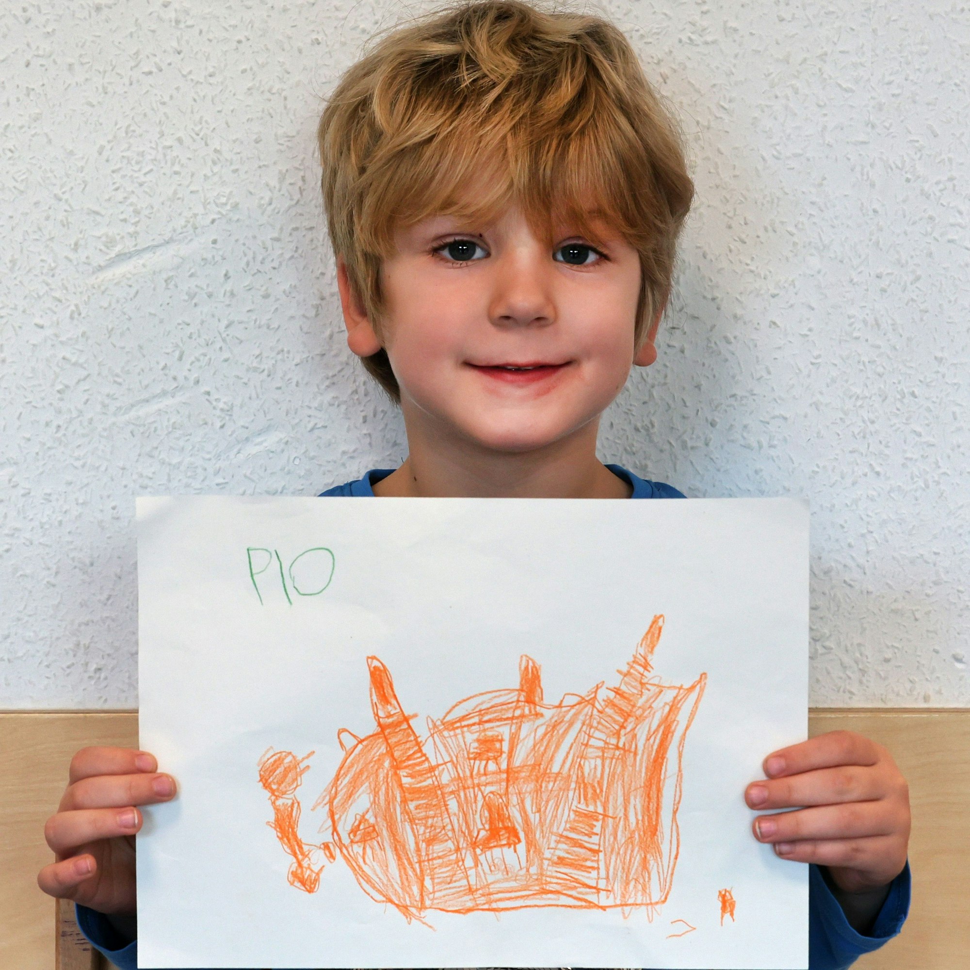 Ein Junge hält einen gemalten Wunschzettel in der Hand und blickt in die Kamera.