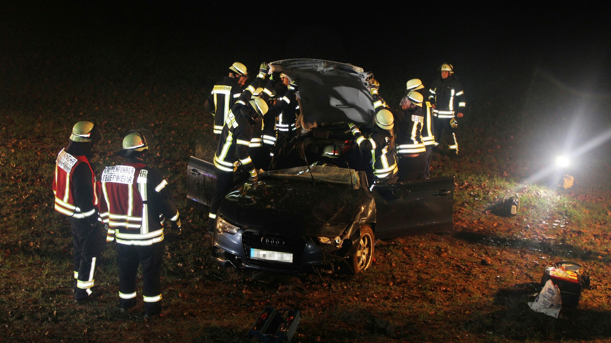 Feuerwehrleute stehen um einen Unfallwagen auf einer Wiese.