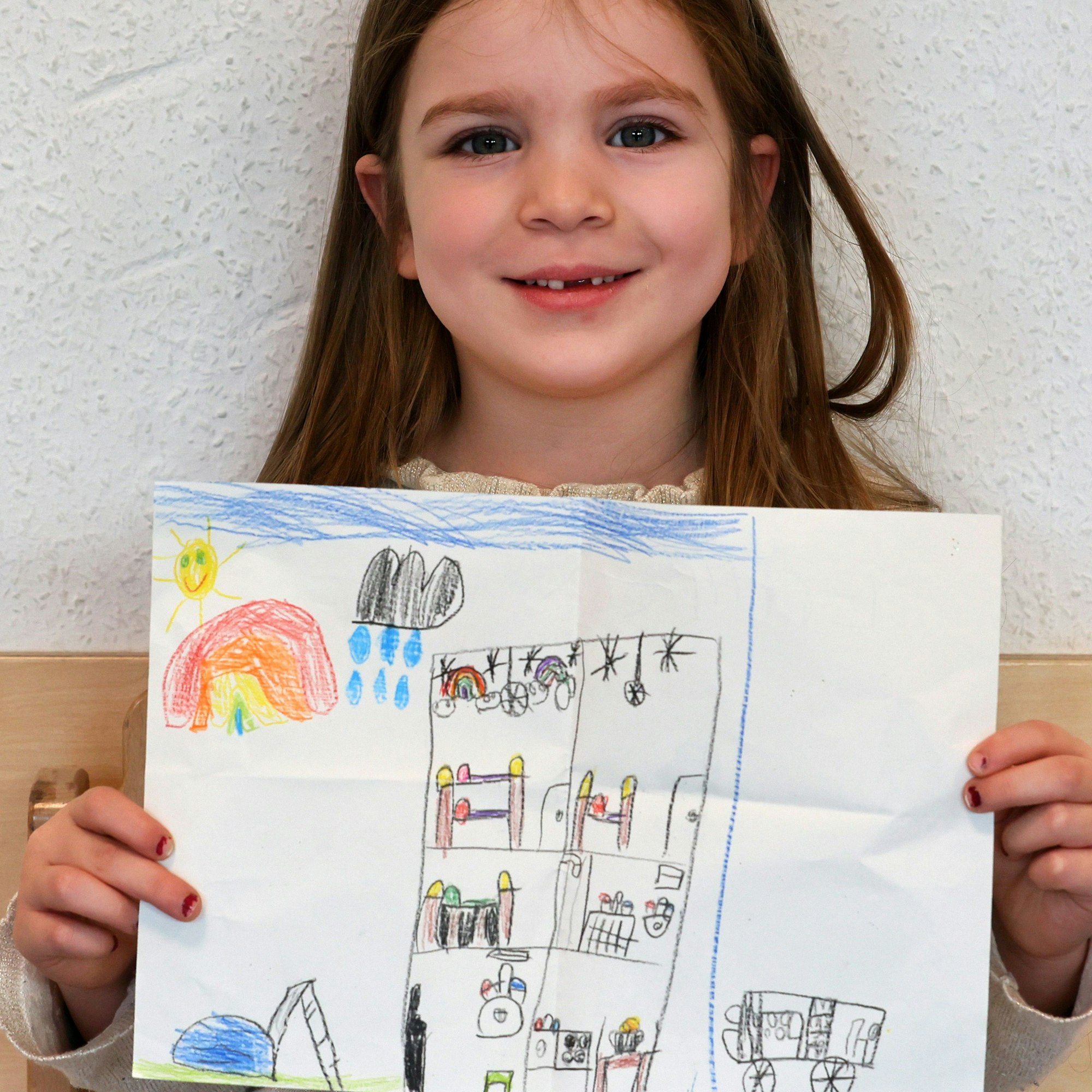 Ein Mädchen hält einen gemalten Wunschzettel in der Hand und blickt in die Kamera.