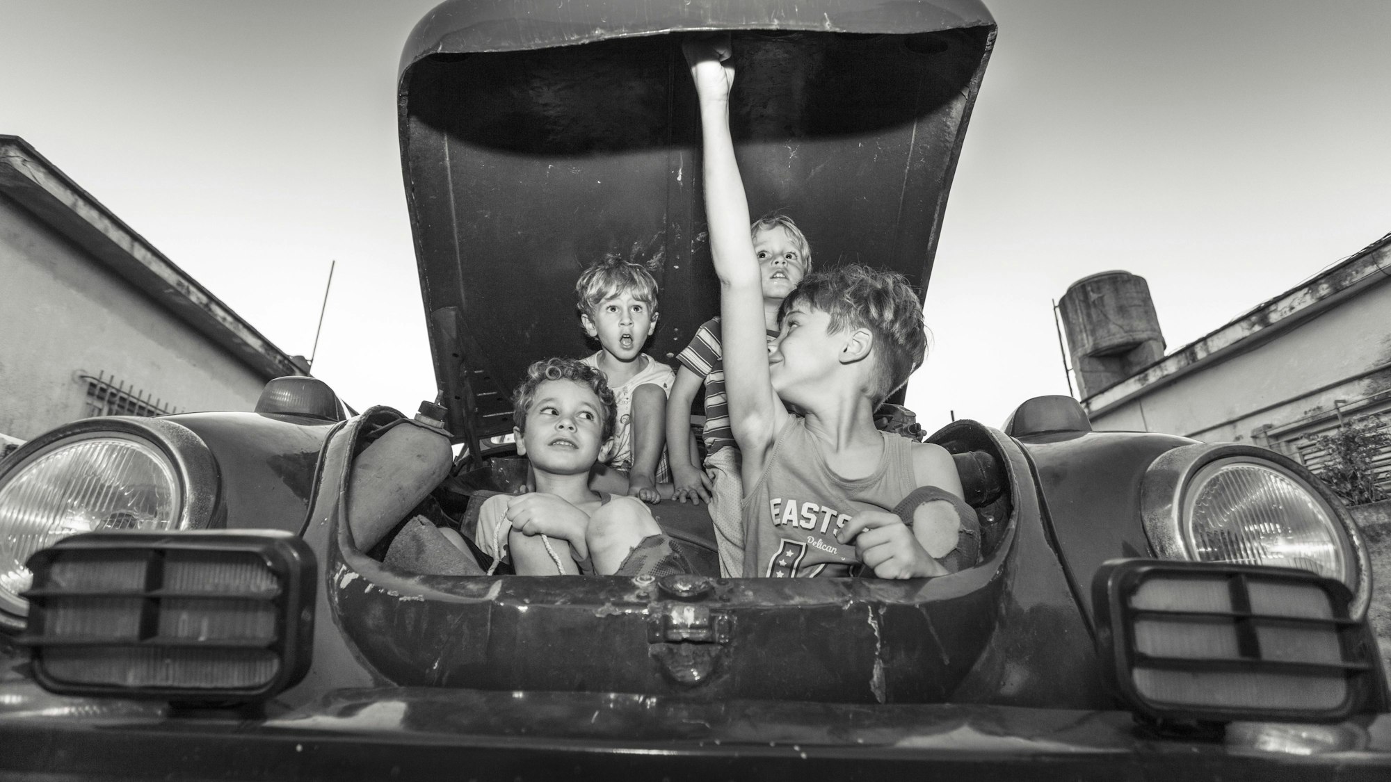 Vier Kinder sitzen im Kofferraum eines alten VW Käfers, eines der Kinder hält den Kofferraumdeckel auf.