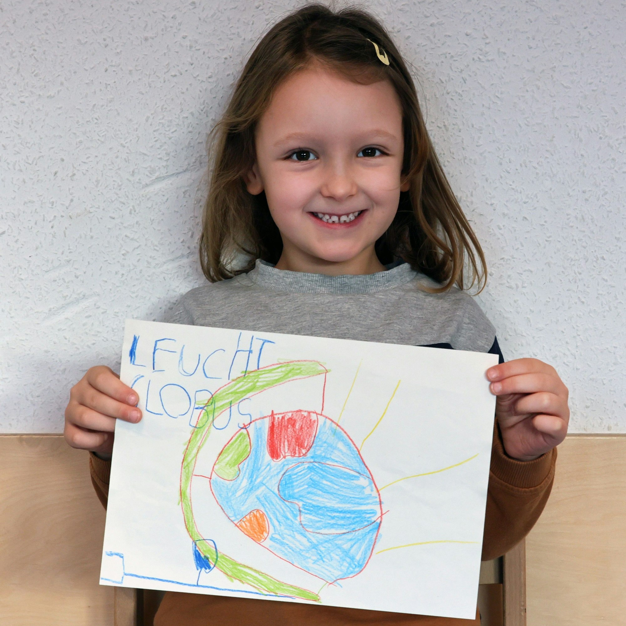Ein Mädchen hält einen gemalten Wunschzettel in der Hand und blickt in die Kamera.