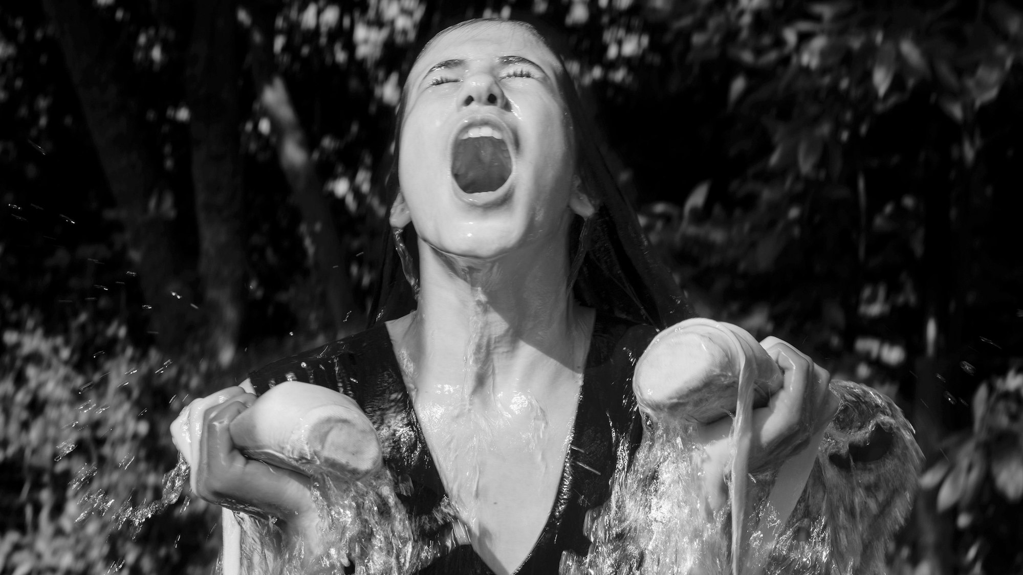 Schwarz-Weiß Fotografie einer jungen Frau, die Ballettschuhe in der hand hält. Sie wird mit Wasser übergossen und hat ihren Mund weit aufgerissen.