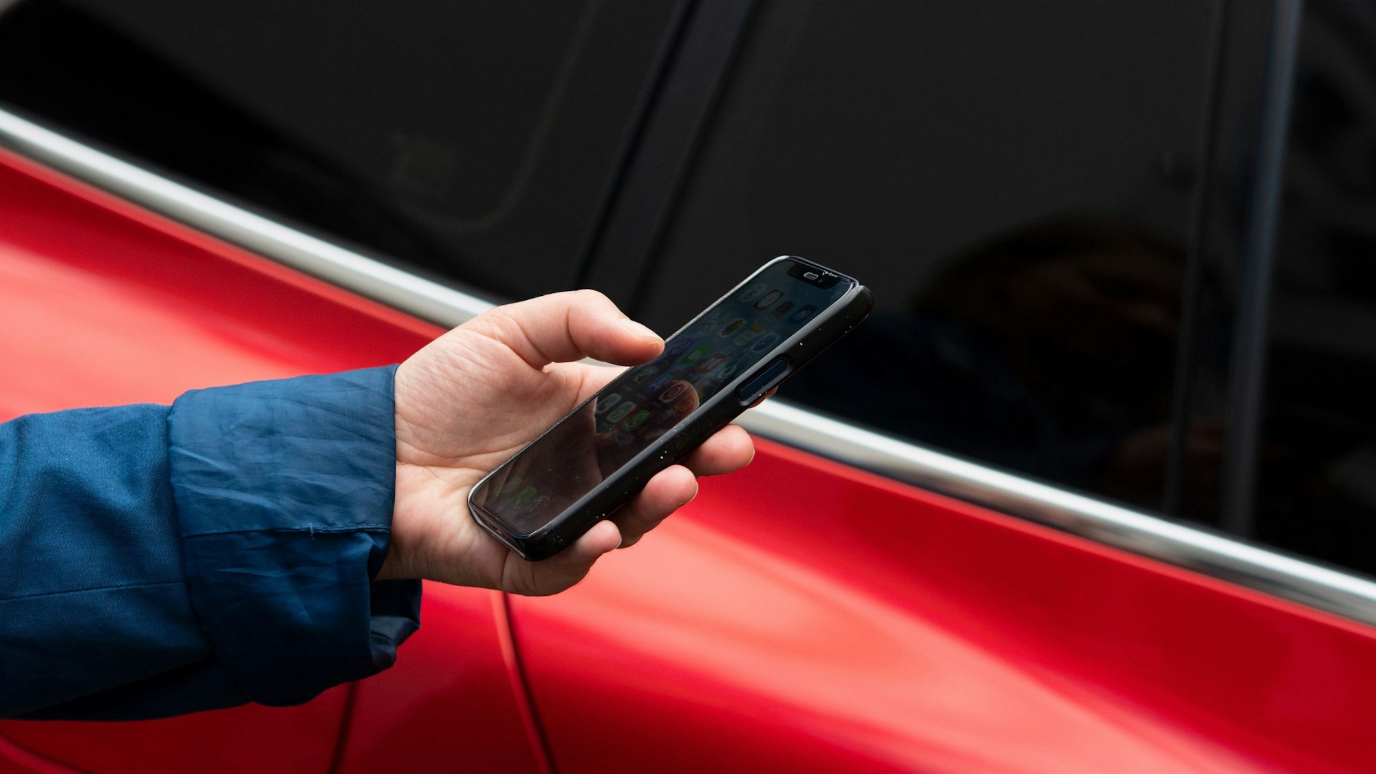 Eine Hand hält ein Smartphone vor einem Auto