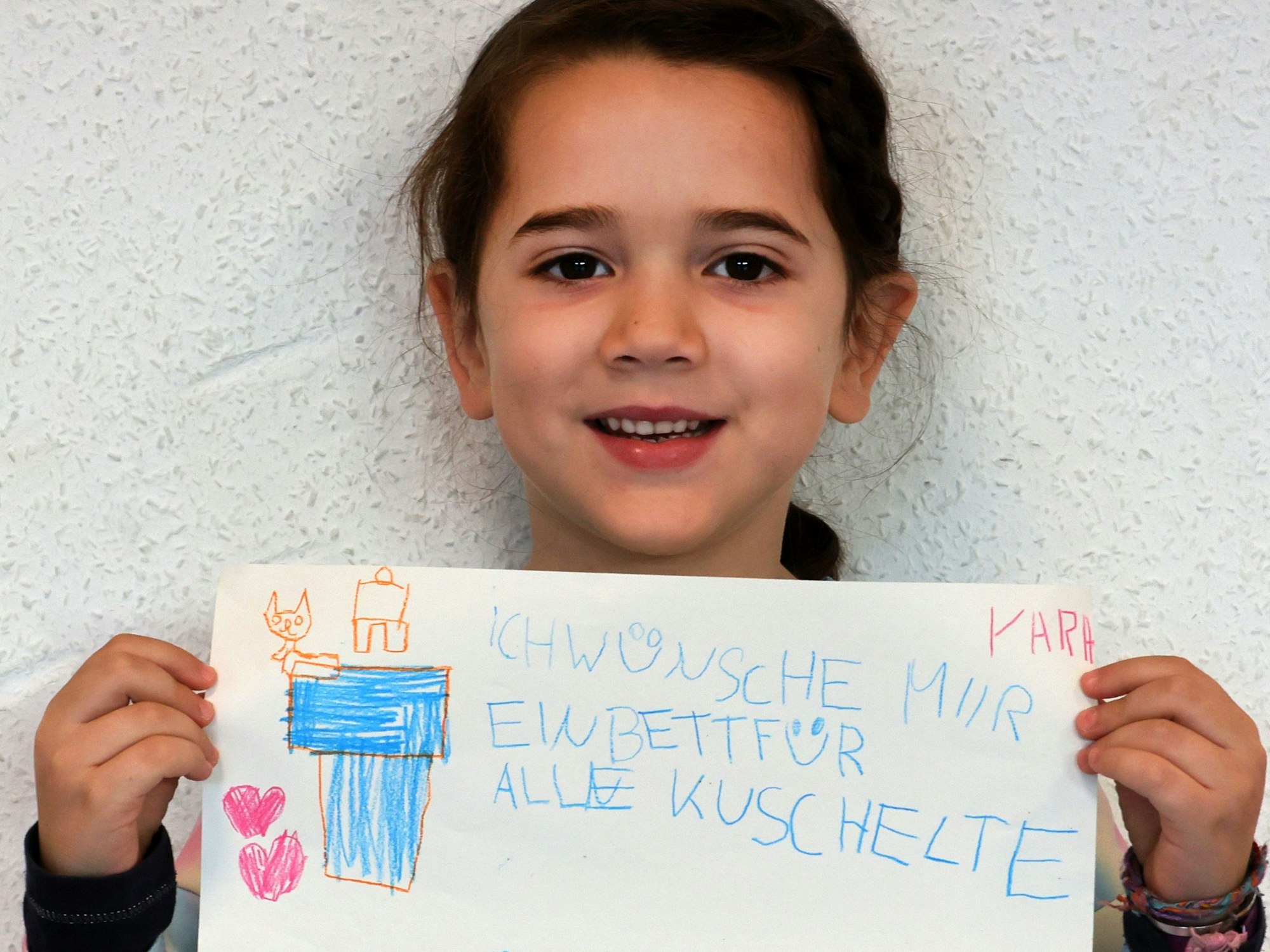 Ein Mädchen hält einen gemalten Wunschzettel in der Hand und blickt in die Kamera.