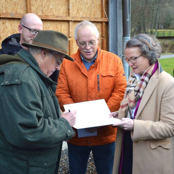 Ditmar Krumpen steht links und unterschreibt den Bescheid. Gegenüber steht die Ministerin für Heimat, Kommunales, Bau und Digitalisierung des Landes Nordrhein-Westfalen Ina Scharrenbach, und Christoph Kammers schaut zu.