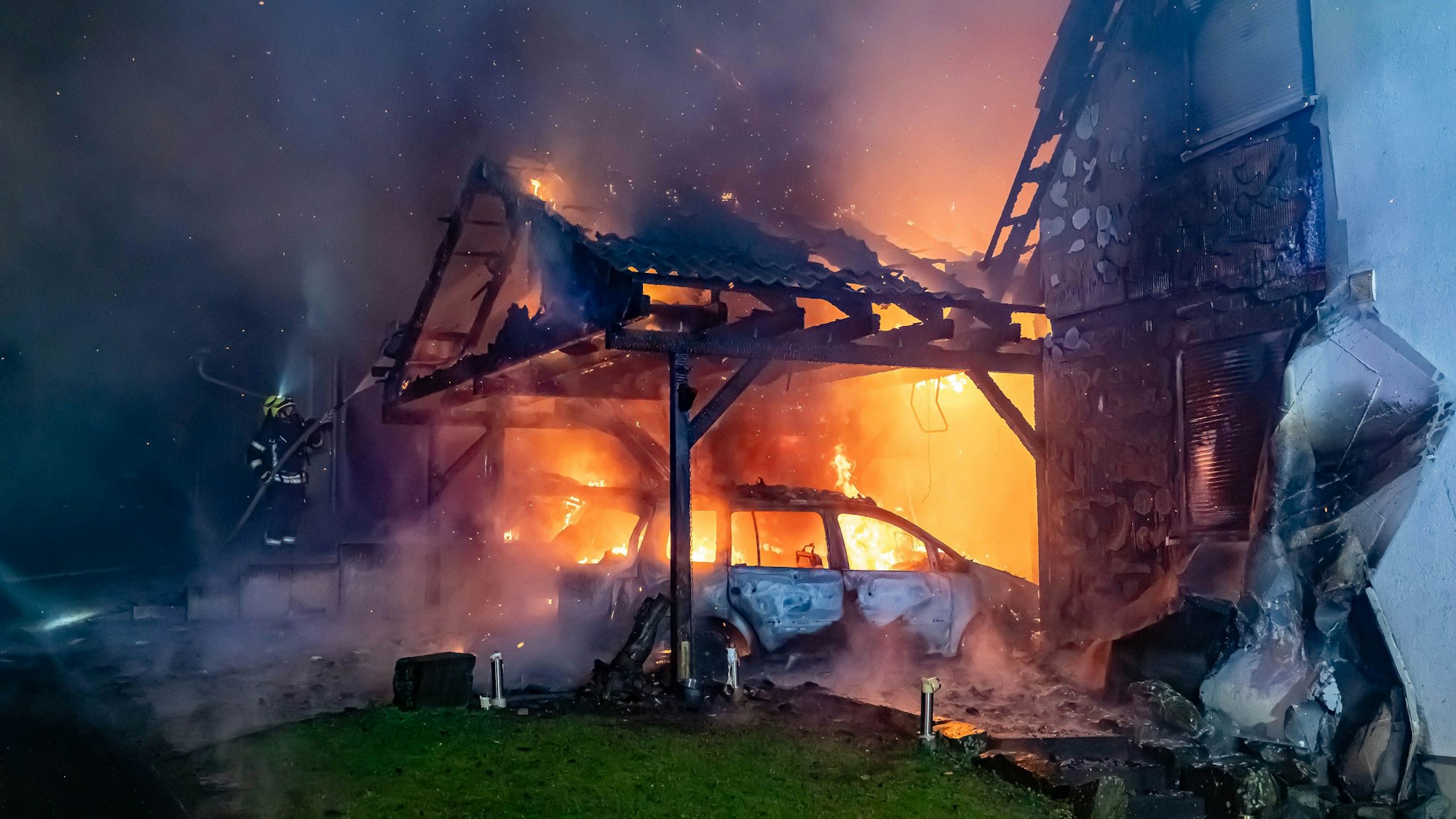 Ein Carport steht in Vollband, ein angrenzendes Haus ist ebenfalls sichtbar Opfer der Flammen geworden.