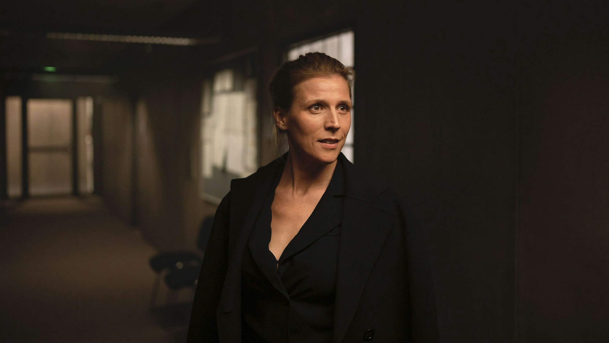 Julia Grosz steht im dunklen Flur eines Büros. Sie trägt schwarze Kleidung.
