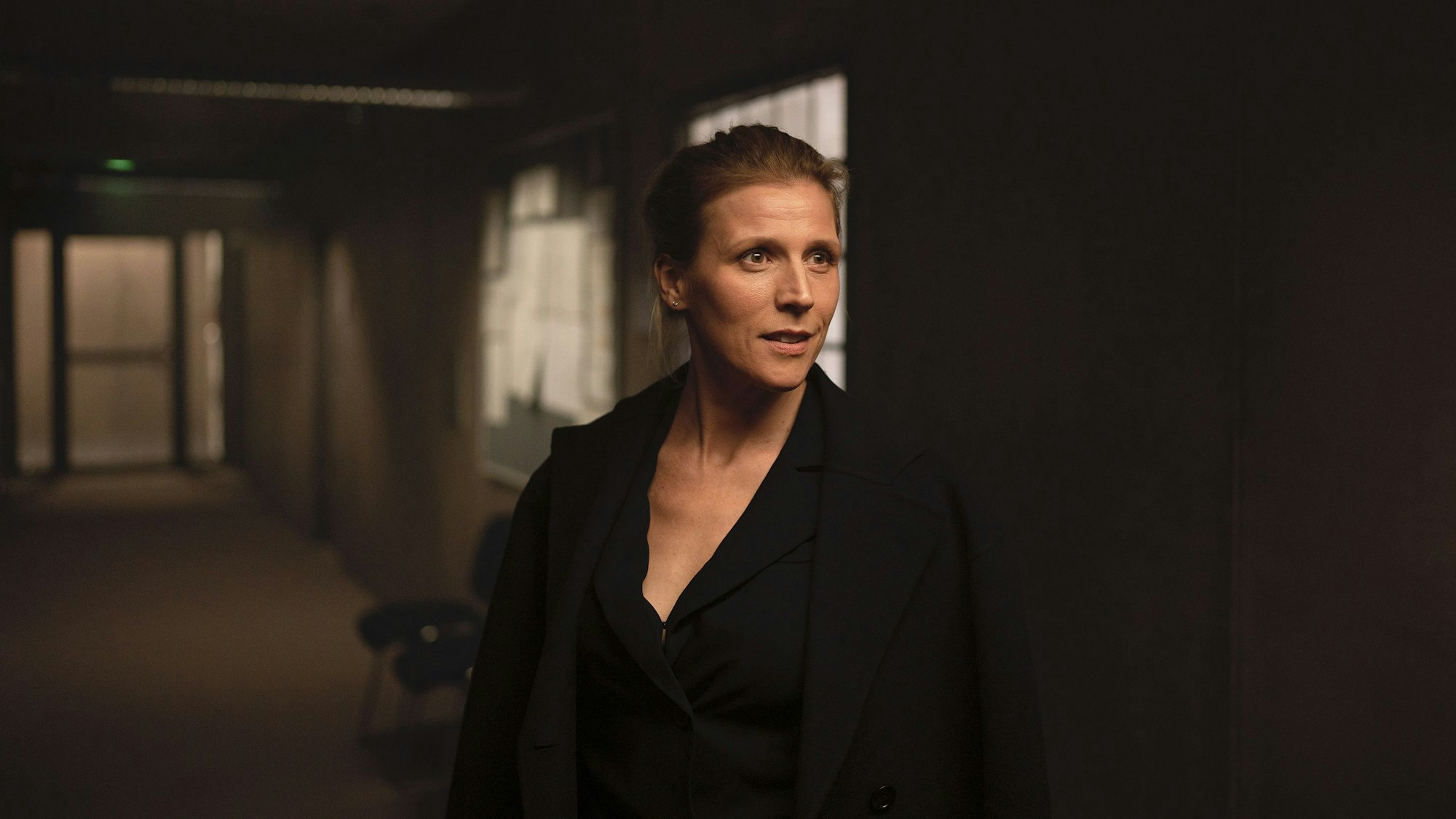 Julia Grosz steht im dunklen Flur eines Büros. Sie trägt schwarze Kleidung.