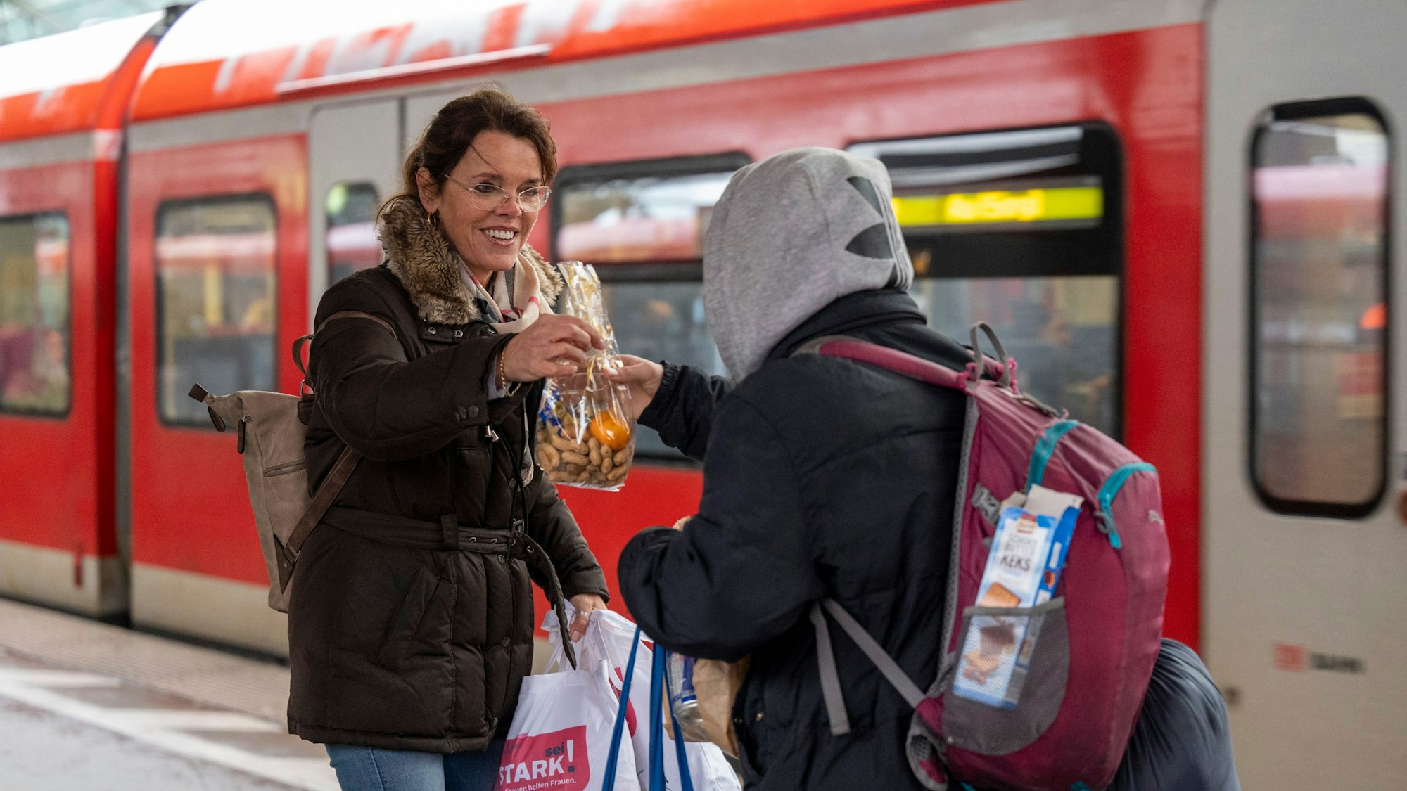 Zu sehen ist eine Frau, die eine Tüte an eine Person mit Rucksack übergibt.