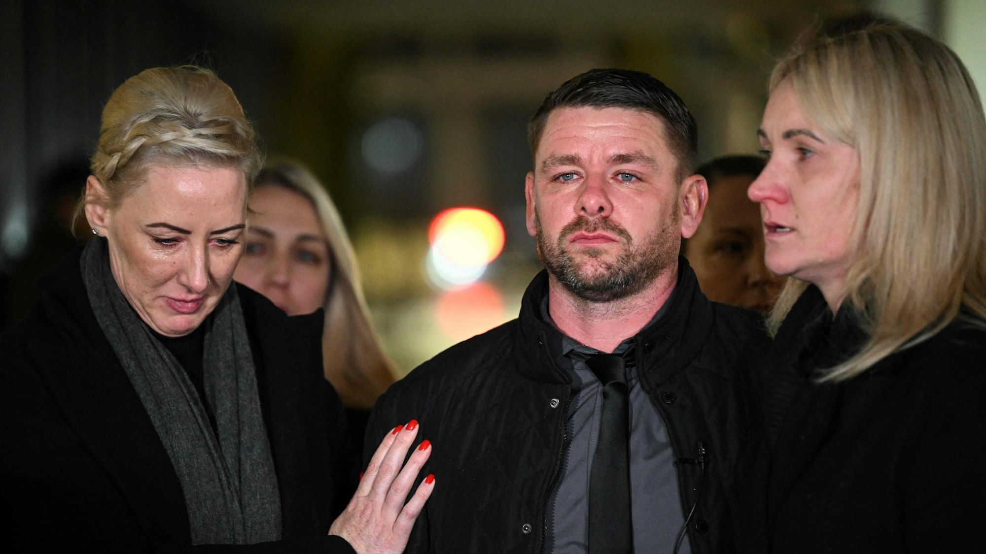 Eine Frau legt einem Mann ihre Hand auf, der traurig in die Ferne blickt.