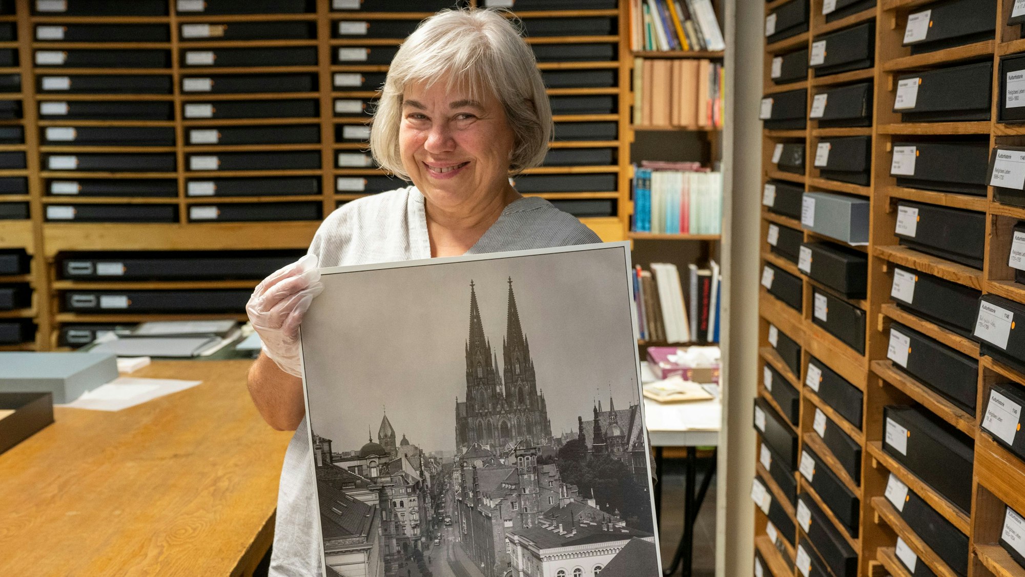 Die Leiterin der Graphischen Sammlung, Rita Wagner, hält ein Schwarz-Weiß-Bild des Kölner Doms in der Hand und schaut in die Kamera.