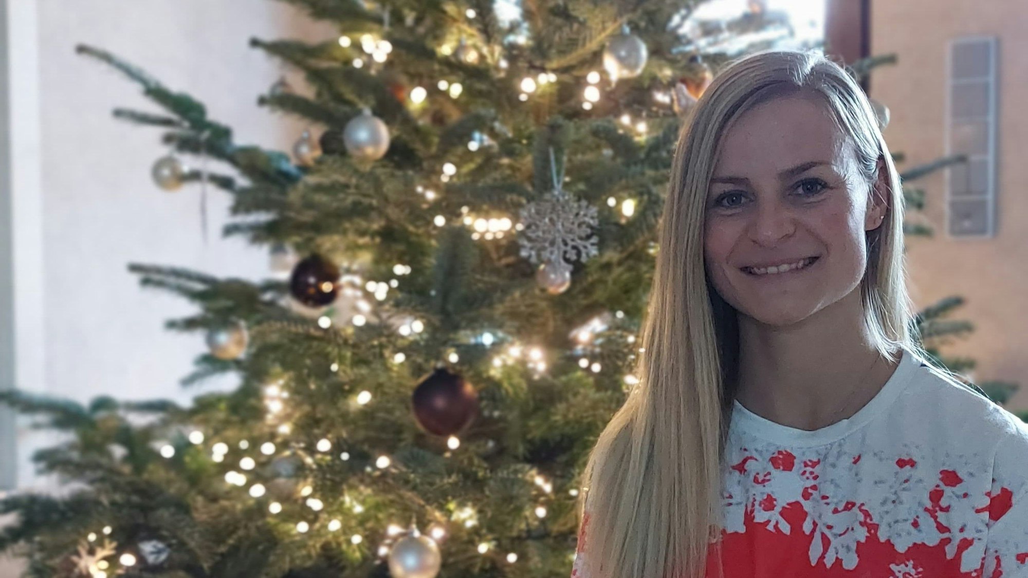 Jessica Rau sitzt in einem Weihnachtspulli vor einem geschmückten Weihnachtsbaum.