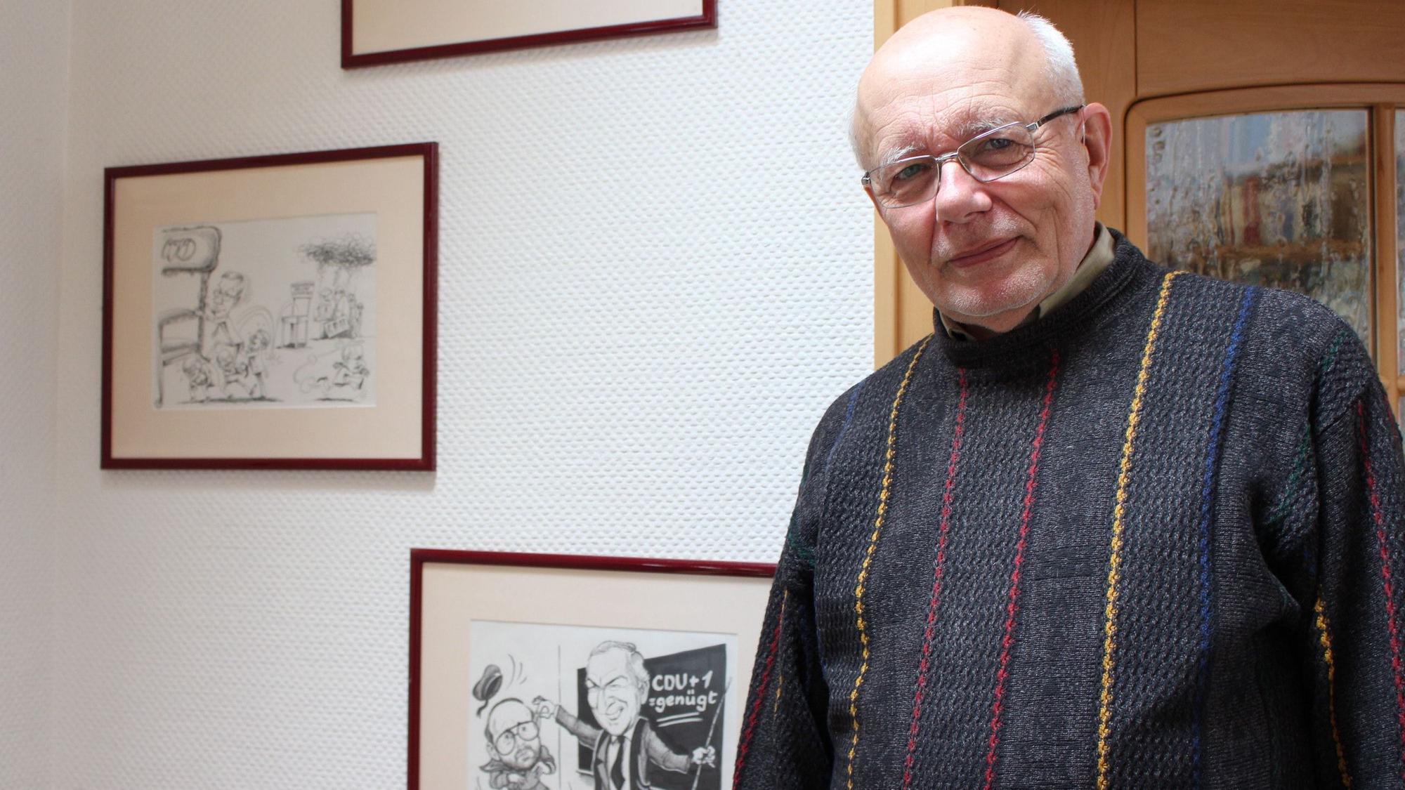 Hans Reiff steht vor einer Wand mit Karikaturen, auf denen er dargestellt wurde.