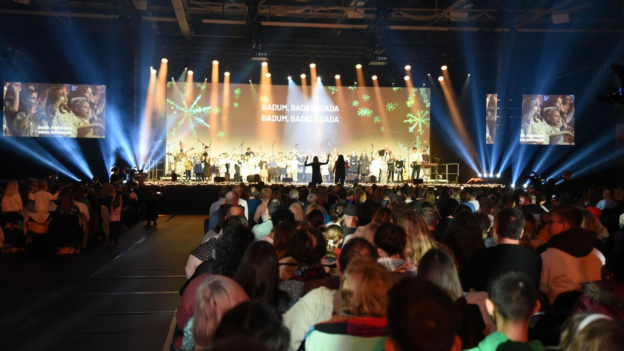 Blick in die volle Schwalbe-Arena. Auf der Bühne ist eine Leinwand, auf der Liedtexte von Weihnachtssongs angezeigt werden.