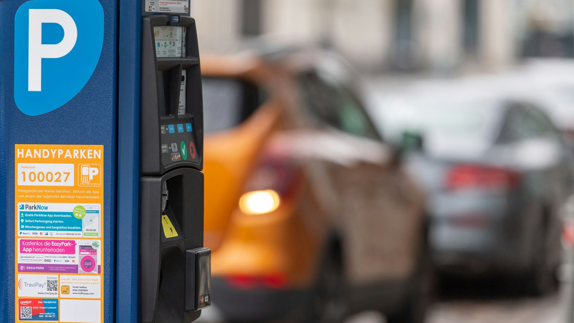 Ein Parkscheinautomat steht am Straßenrand. Im Hintergrund Autos.