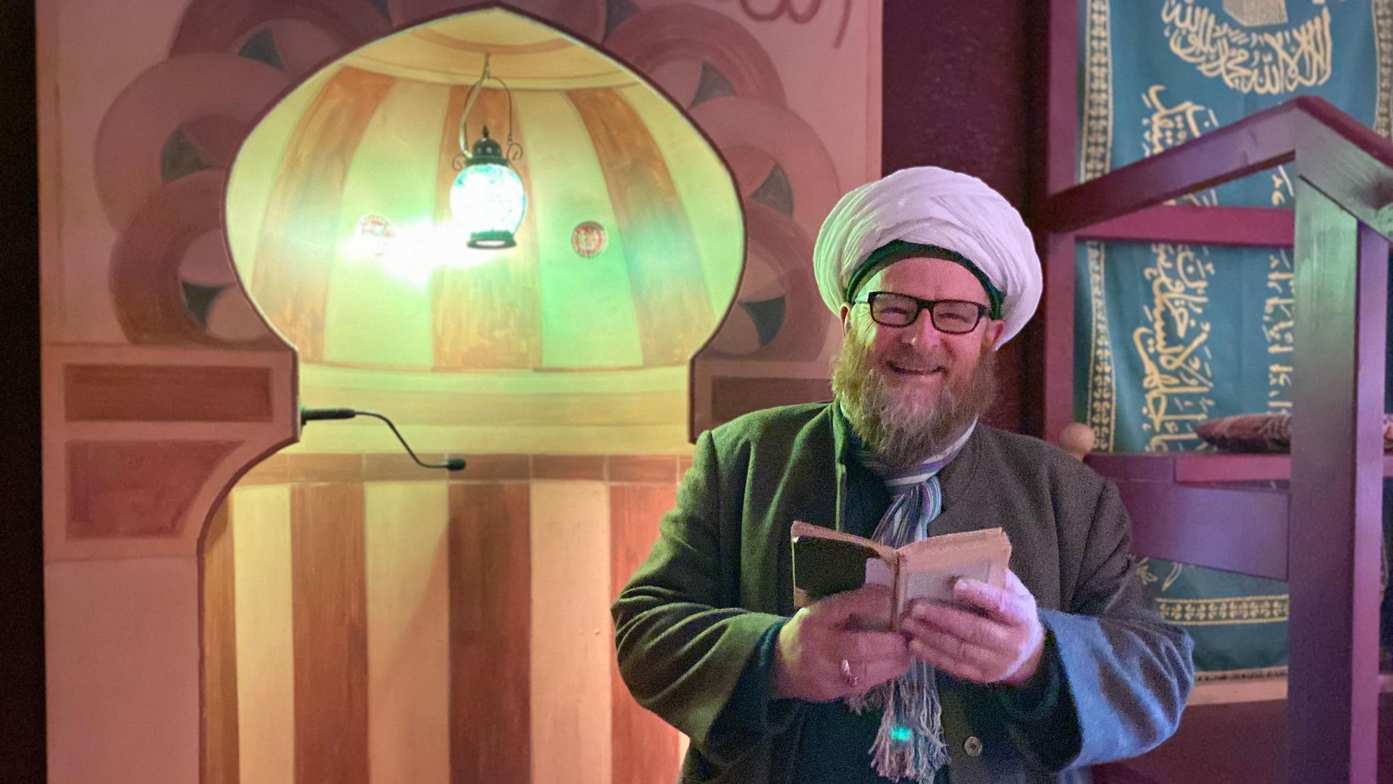 Ahmad Adamek trägt Gebetsmütze und Turban. Er liest in der osmanischen Herberge in Kall-Sötenich aus dem Koran.