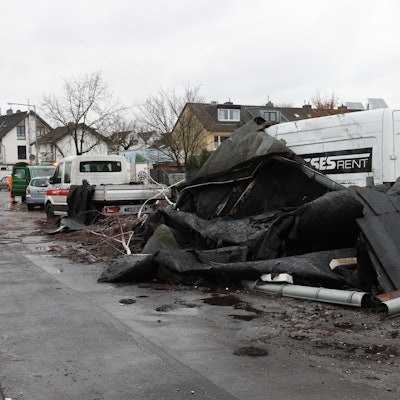 Ein abgedecktes Dach ist auf eine Straße in Köln-Poll geweht worden und liegt vor einem Kleintransporter.