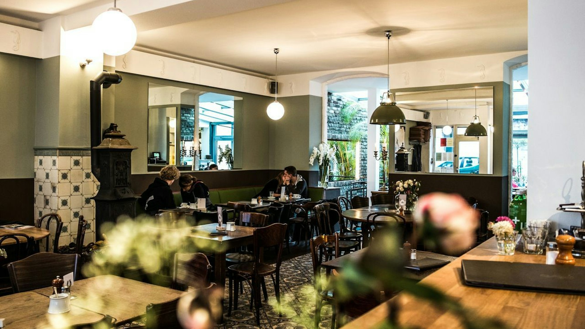 Das Café Sehnsucht in Ehrenfeld mit altem Bollerofen vor grüner Wand und dunklen Holzstühlen.