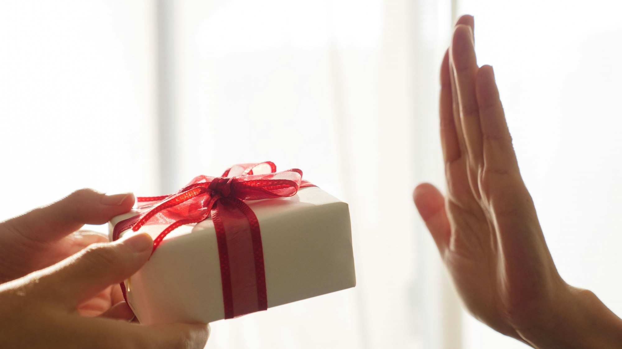 Zwei Hände halten ein Geschenkpäckchen, eine Hand ist abwehrend nach oben gereckt.