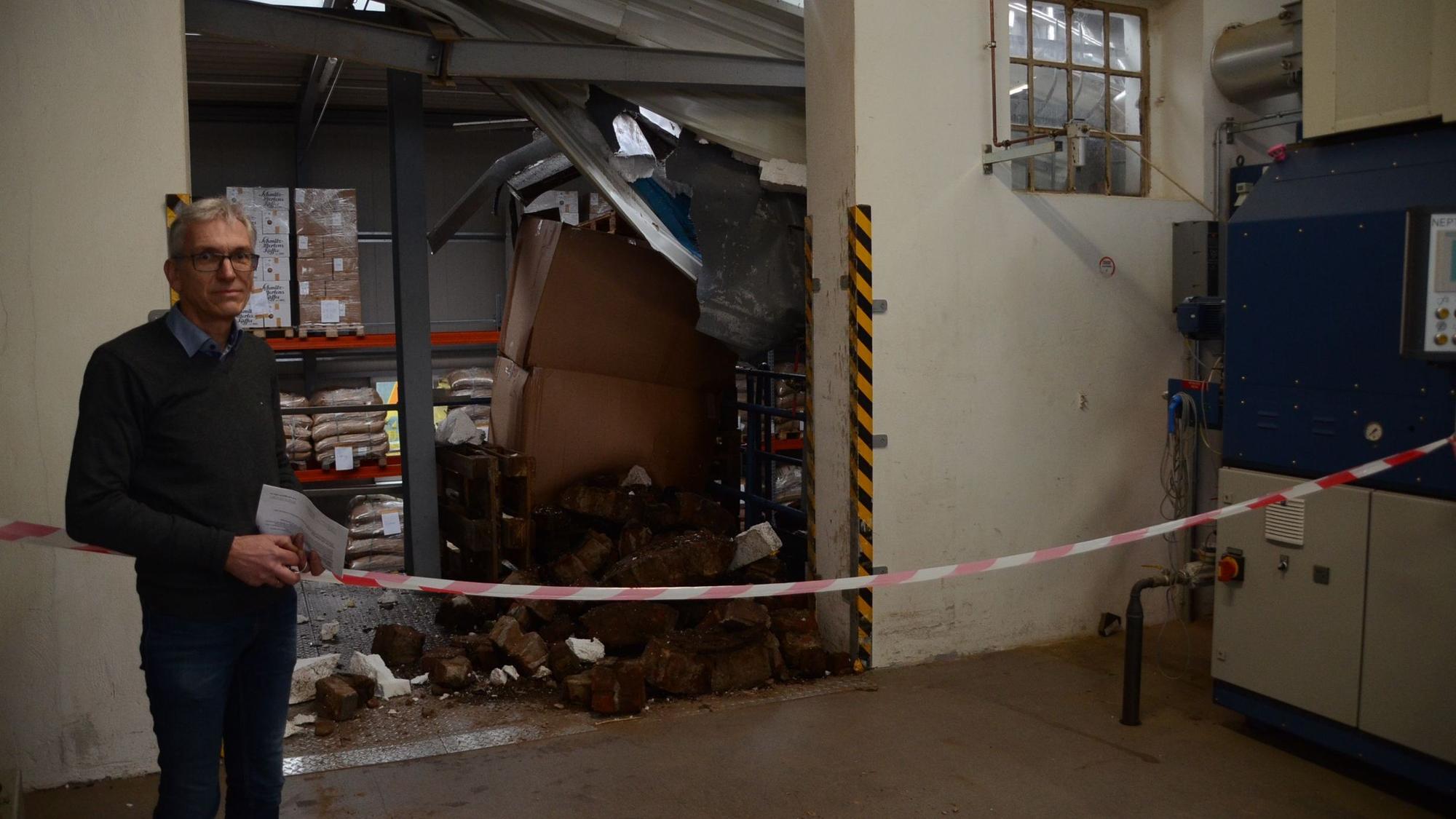 Ein Mann mit Brille und grauen Hallen steht vor einem Haufen an Backsteinen und verbogenem Metall.