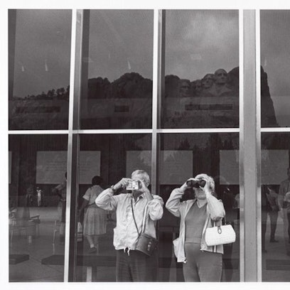 Menschen fotografieren den Mount Rushmore durch eine Glasscheibe hindurch.