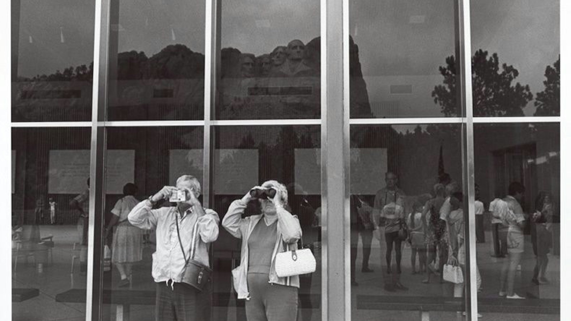Menschen fotografieren den Mount Rushmore durch eine Glasscheibe hindurch.