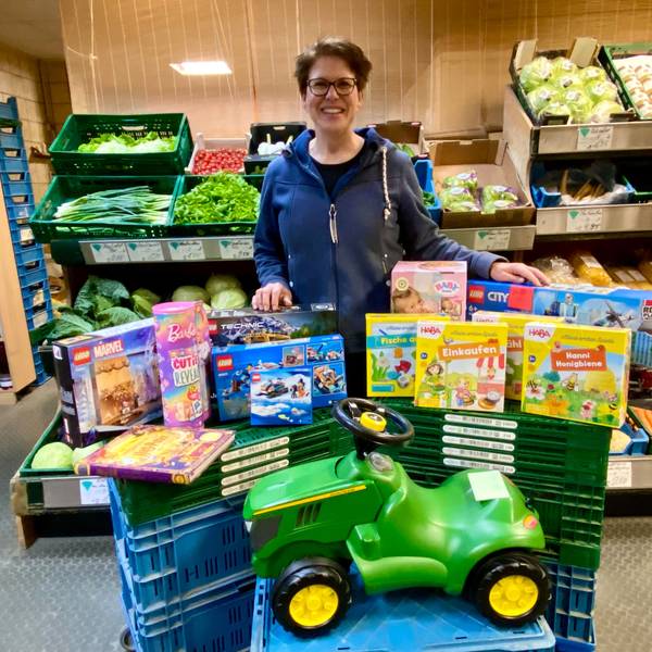 Zu sehen ist eine Frau mit vielen Geschenken, darunter ein grünes Bobby Car.