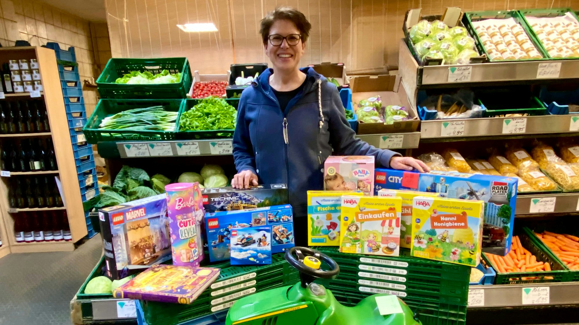 Zu sehen ist eine Frau mit vielen Geschenken, darunter ein grünes Bobby Car.