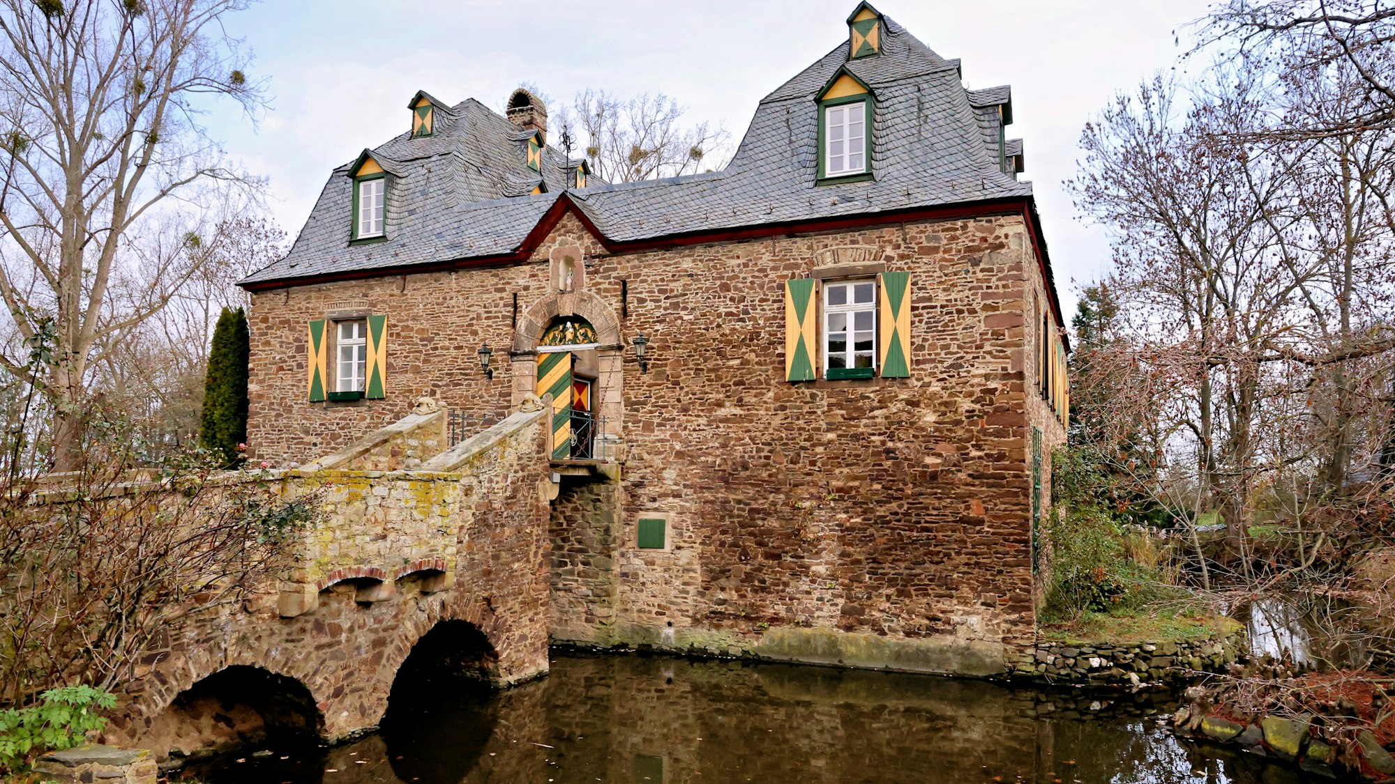Blick über den Wassergraben hinweg auf das Herrenhaus, links die Brücke und die herabgelassene Zugbrücke.