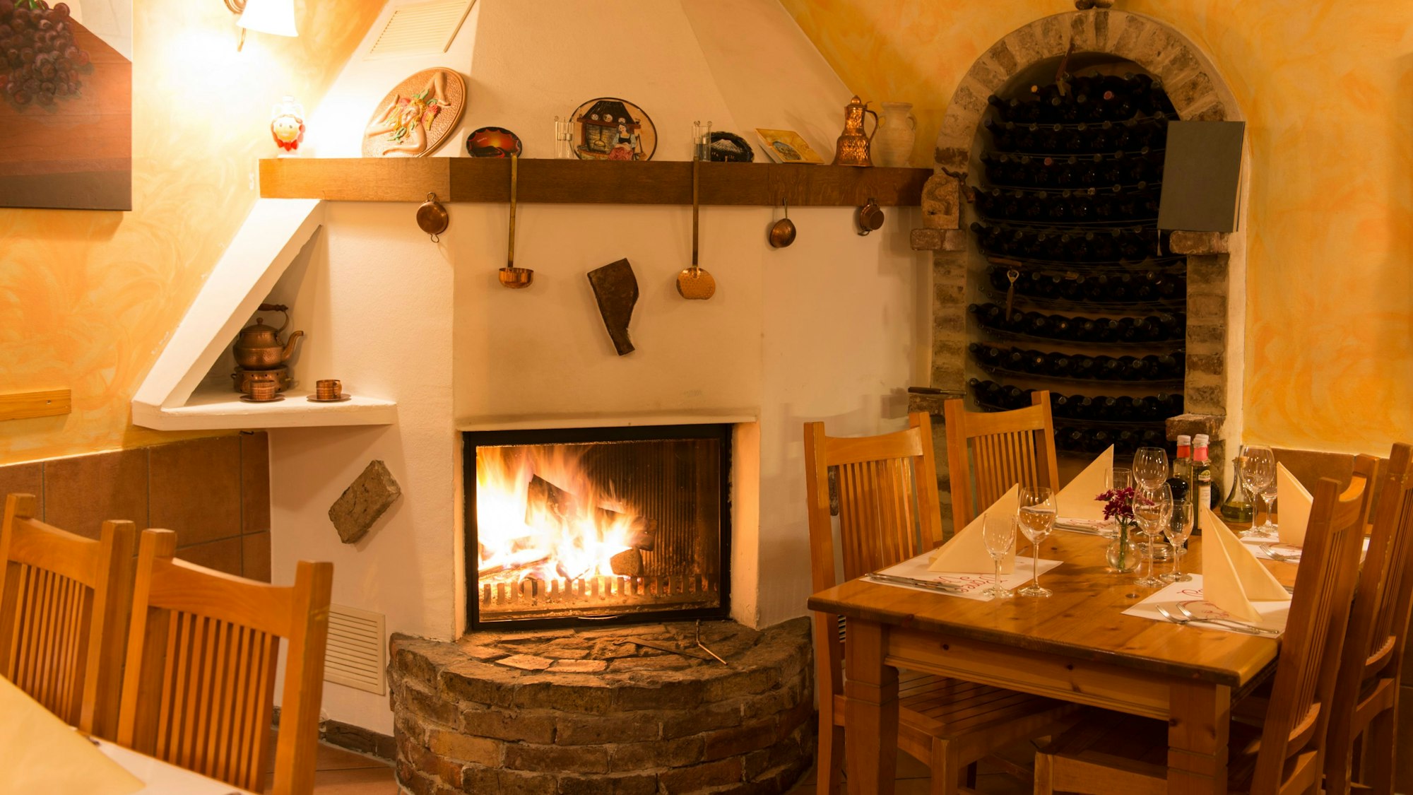 Ein rustikaler Kamin mit Steinvorbau zwischen Holztischen, geschmückt mit Suppenkellen und Tontellern.