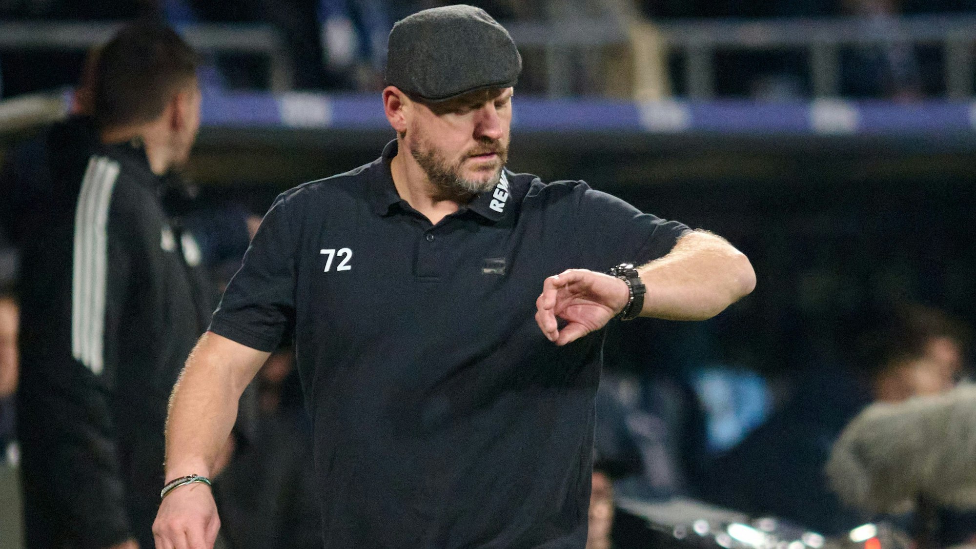 Während der Bundesliga-Begegnung VfL Bochum gegen 1. FC Köln am 11. November 2023 schaut Kölns Trainer Steffen Baumgart am Spielfeldrand auf seine Armbanduhr. Er trägt Schirmmütze und ein schwarzes T-Shirt.