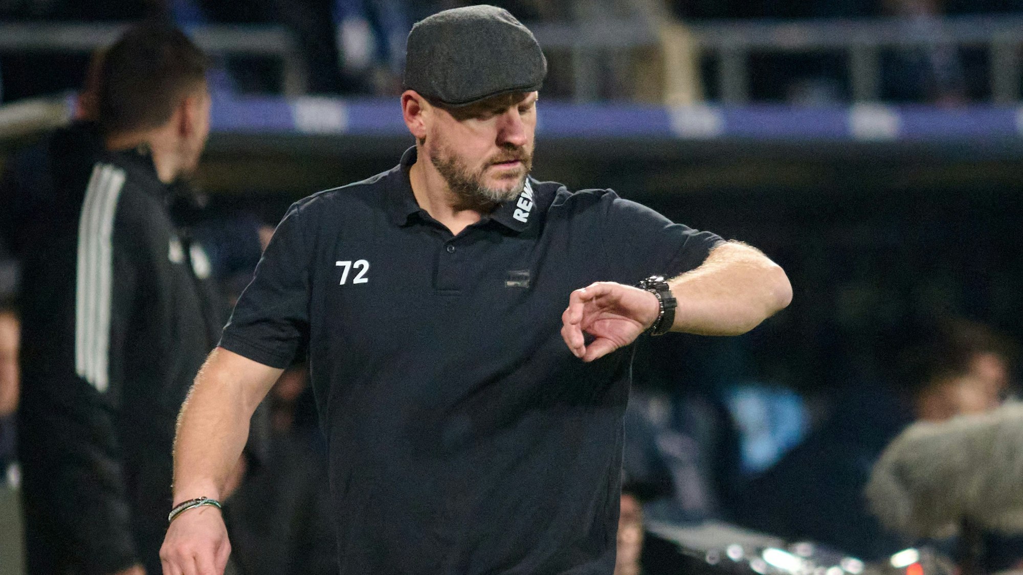 Während der Bundesliga-Begegnung VfL Bochum gegen 1. FC Köln am 11. November 2023 schaut Kölns Trainer Steffen Baumgart am Spielfeldrand auf seine Armbanduhr. Er trägt Schirmmütze und ein schwarzes T-Shirt.